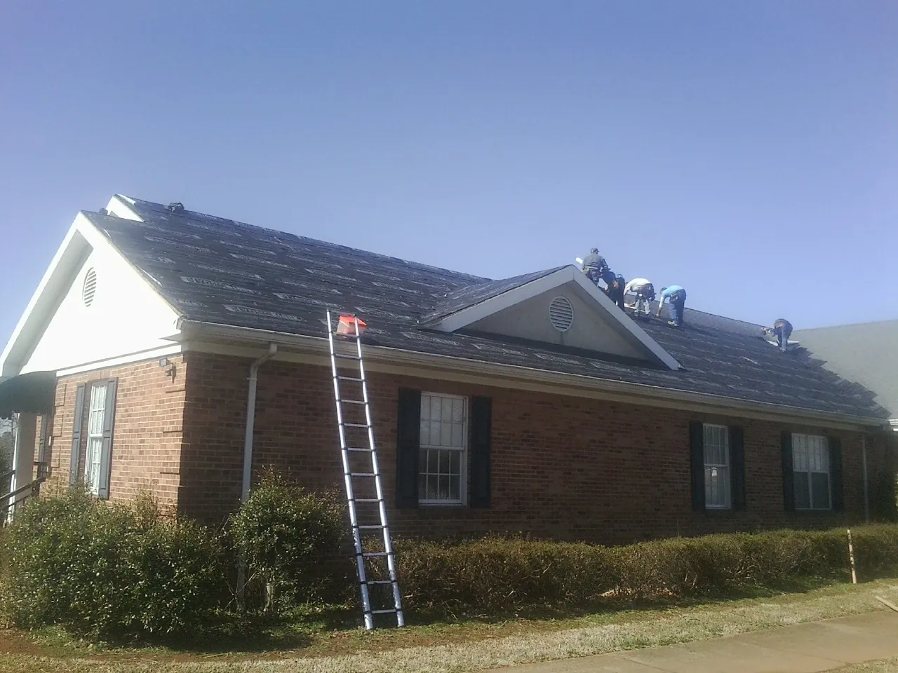Crew tearing shingles off a brick ranch roof with a ladder set — Emergency Roof Repair work by our crew in Fullerton